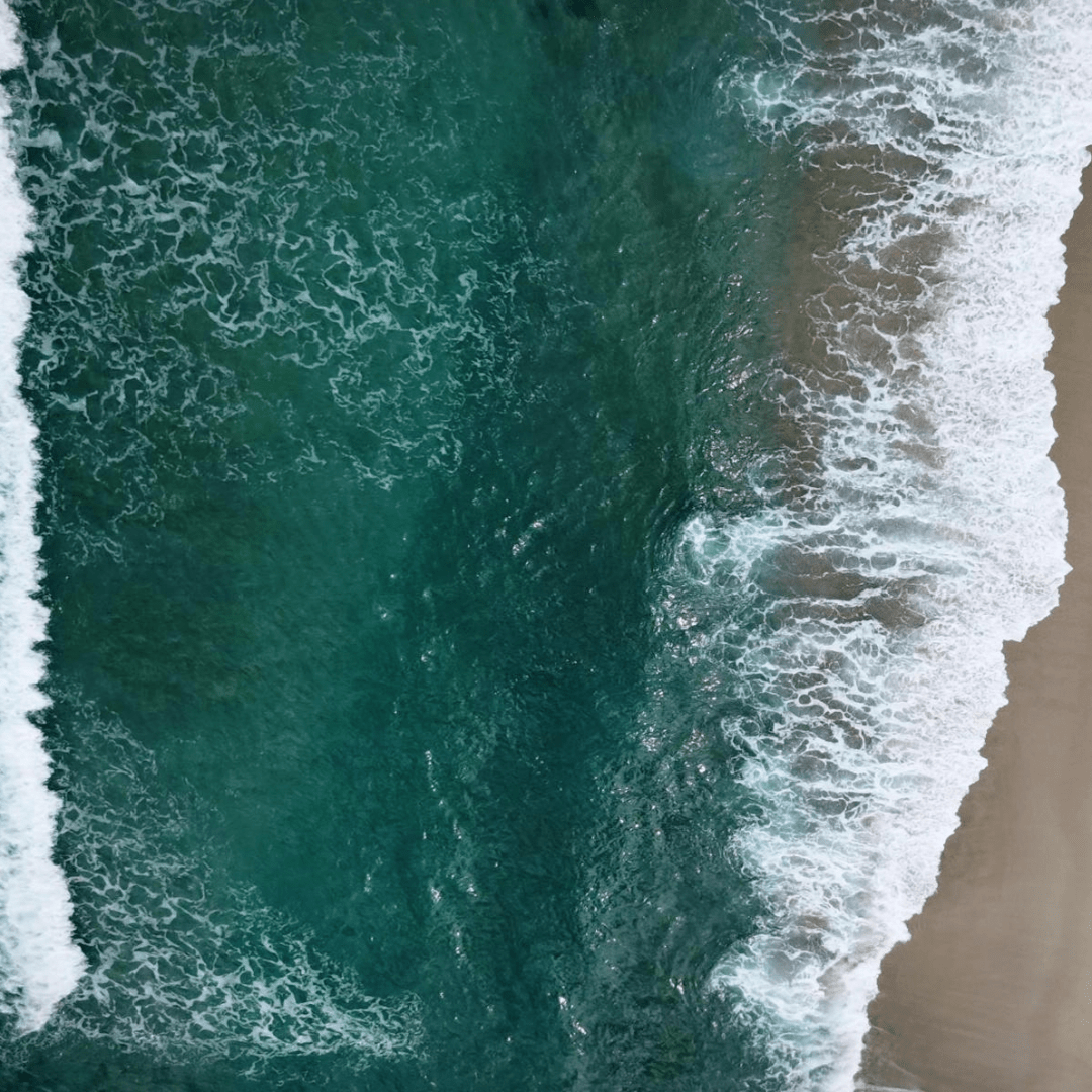 Looking down on the ocean as it meets a sandy beach at high tide.